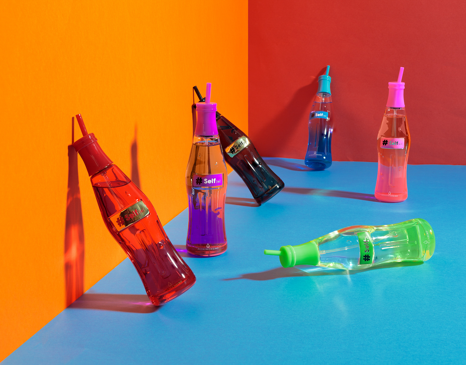 Garrafas de perfumes coloridas em formato de garrafa de refrigerante ambientada em fundo colorido, fotografia publicitária por Gilson Reis Fotografia.