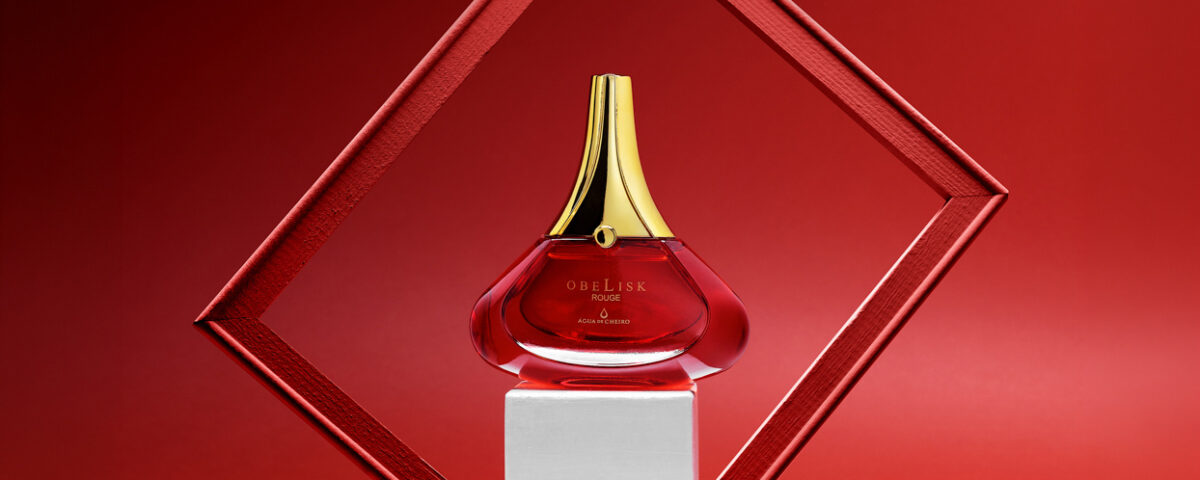 Foto de perfume de frasco vermelho e tampa dourada com moldura e fundo vermelho. Por Gilson Reis Fotografia.