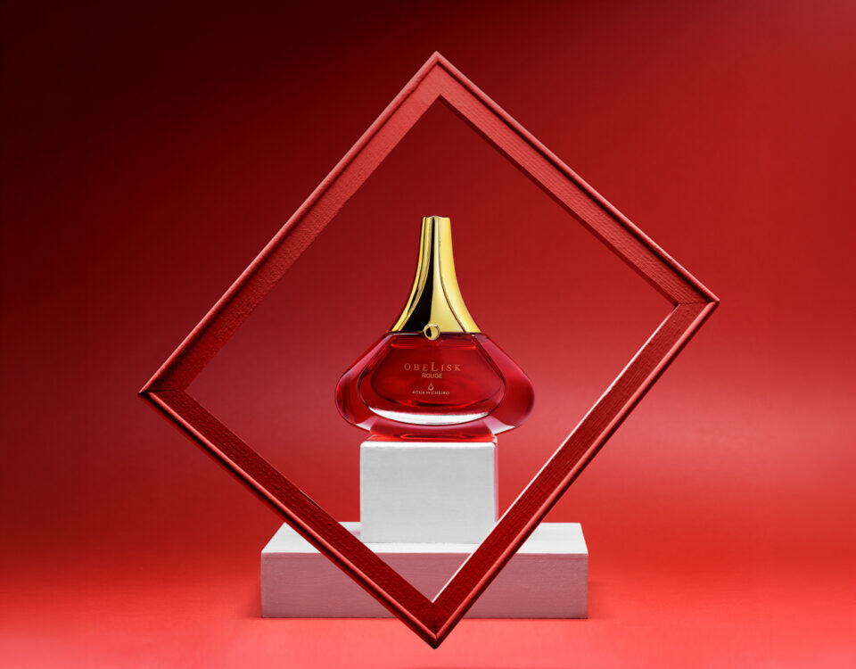 Foto de perfume de frasco vermelho e tampa dourada com moldura e fundo vermelho. Por Gilson Reis Fotografia.