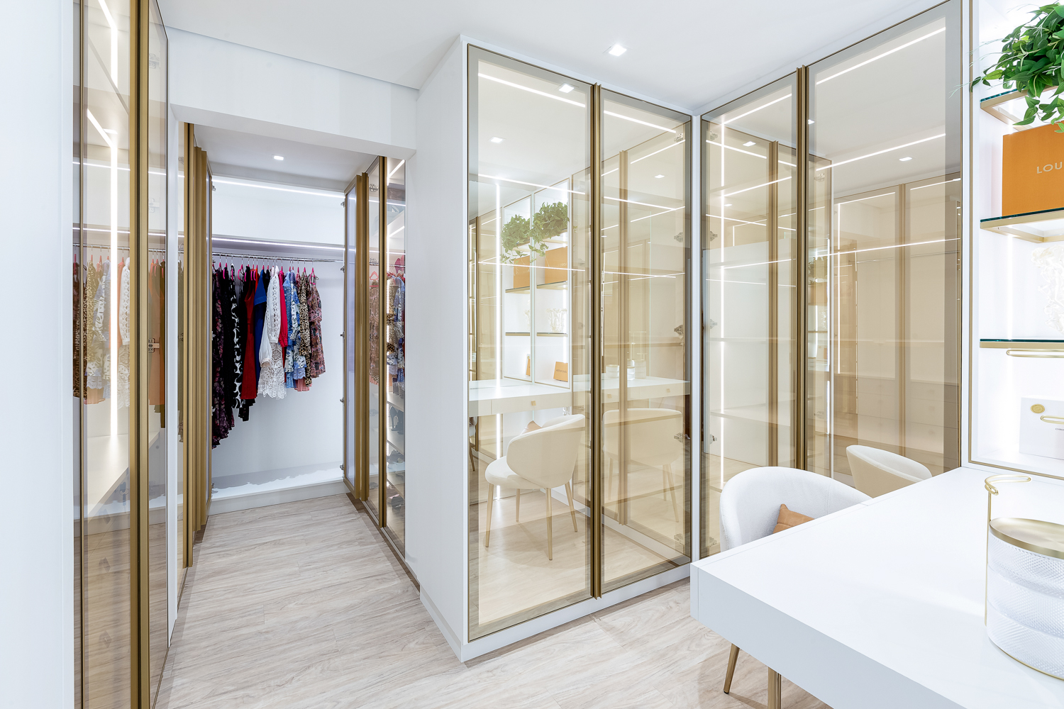 Closet integrado à suíte com armários claros, portas de vidro e circulação iluminada.