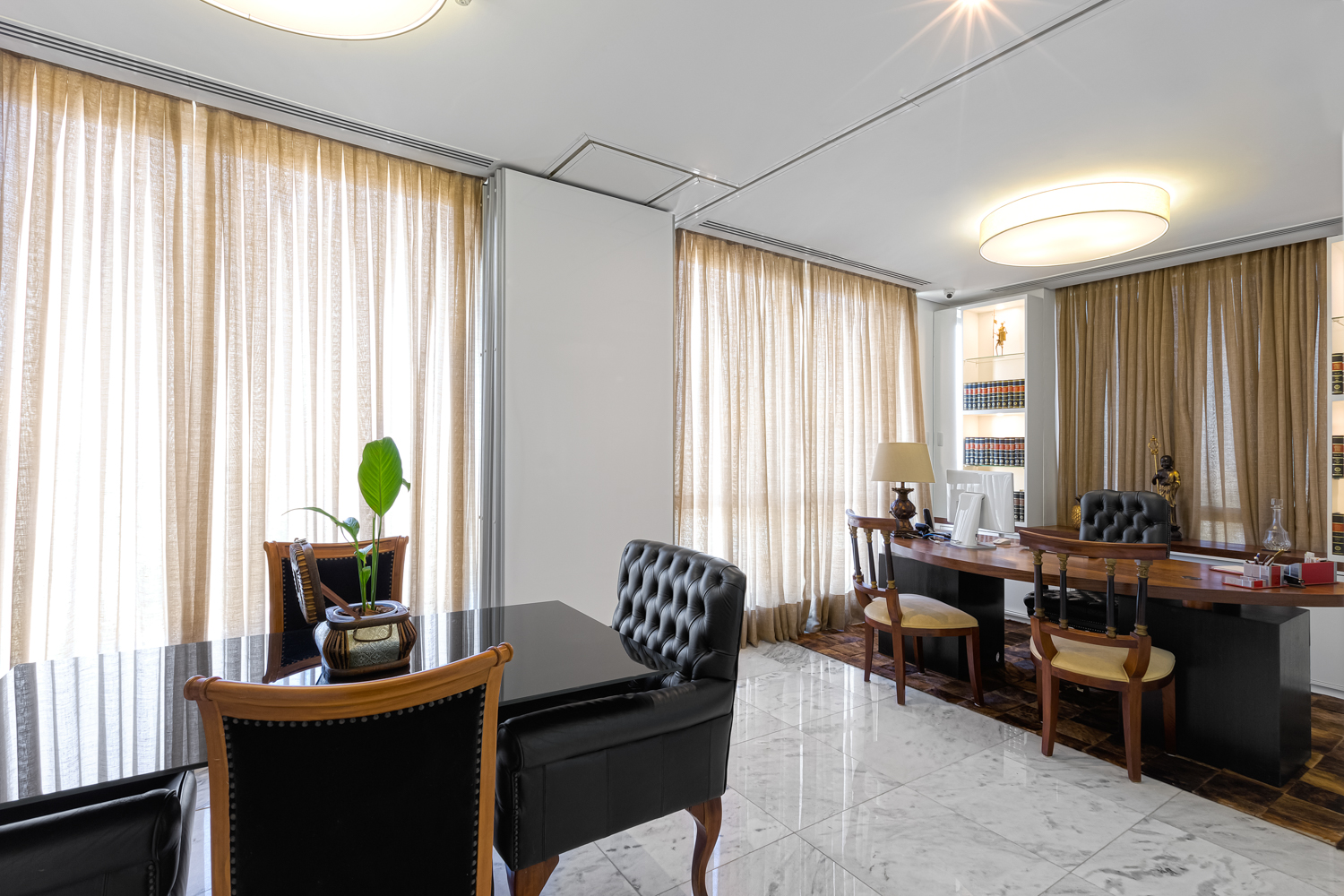 Escritório residencial com mesa de trabalho, poltronas e iluminação natural lateral.