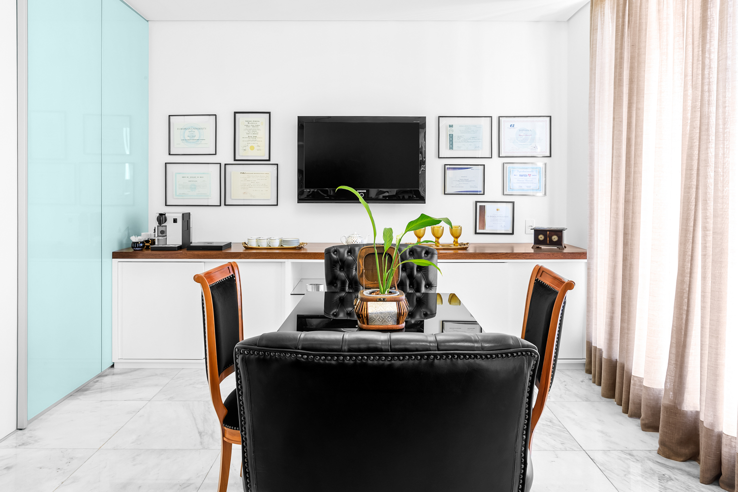 Home office com mesa, cadeira, painel de televisão e quadros organizados na parede.