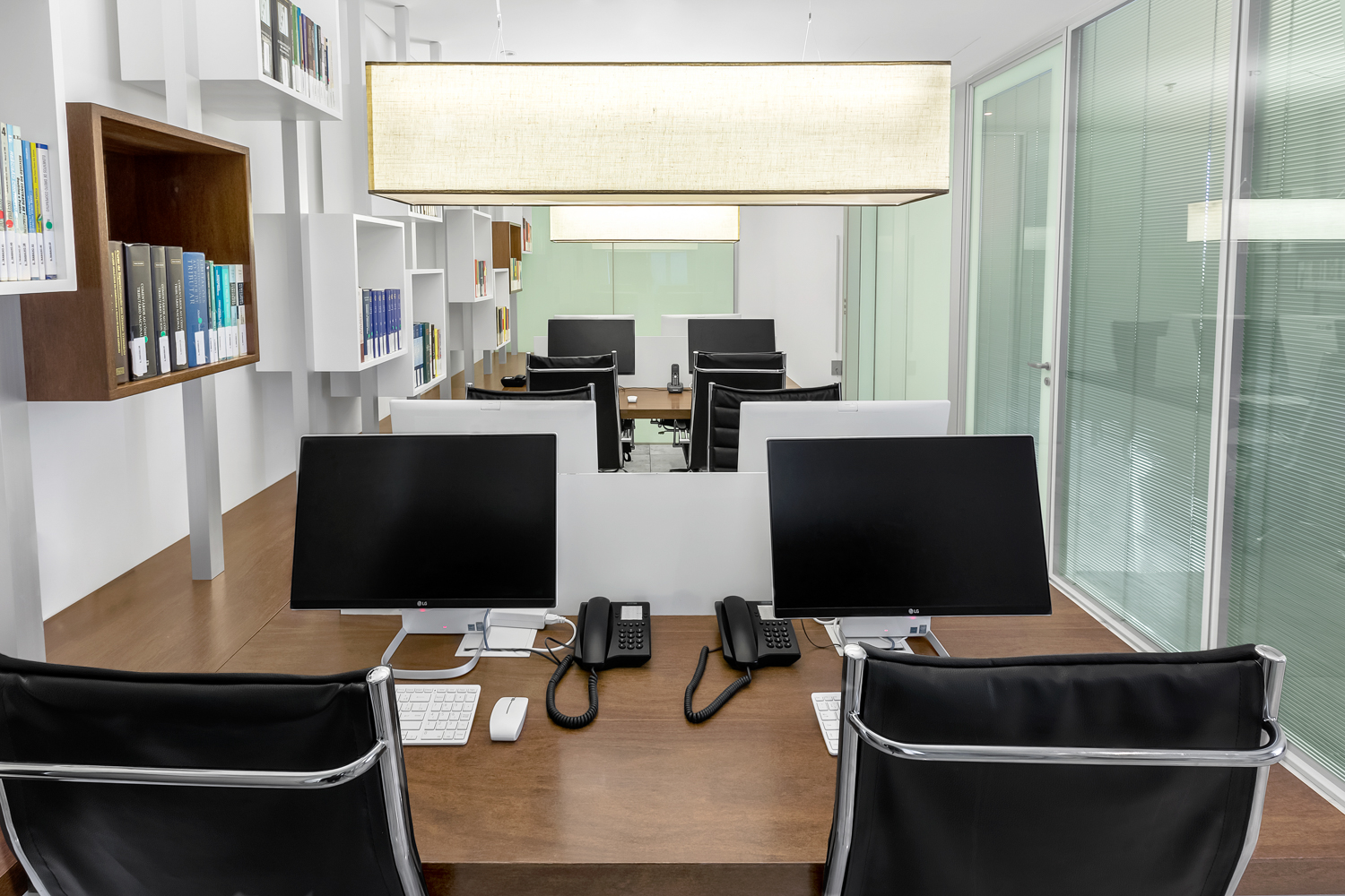 Escritório corporativo com estações de trabalho, divisória de vidro e iluminação natural.