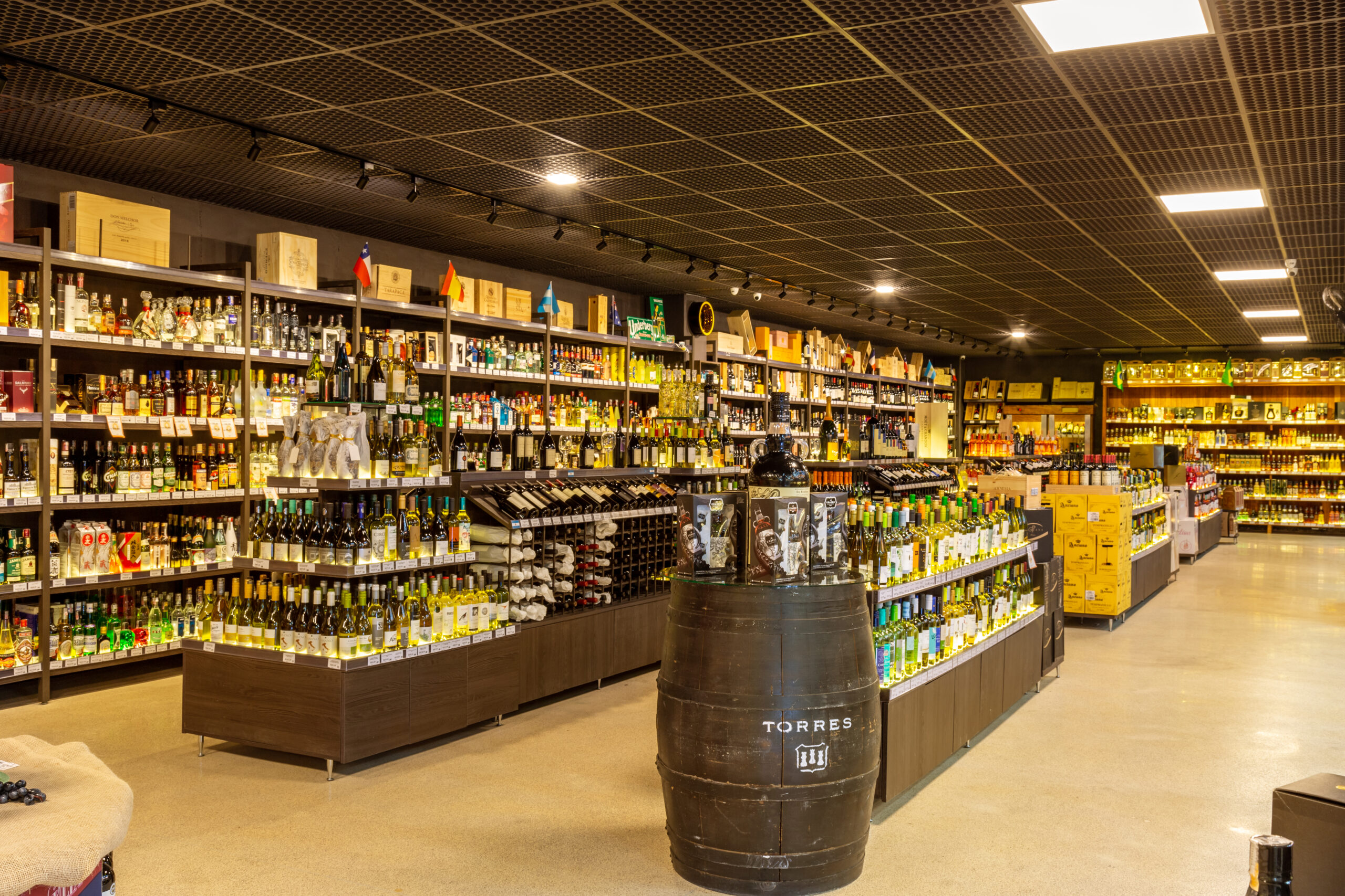 Interior de empório com prateleiras de bebidas, madeira escura e iluminação aconchegante.