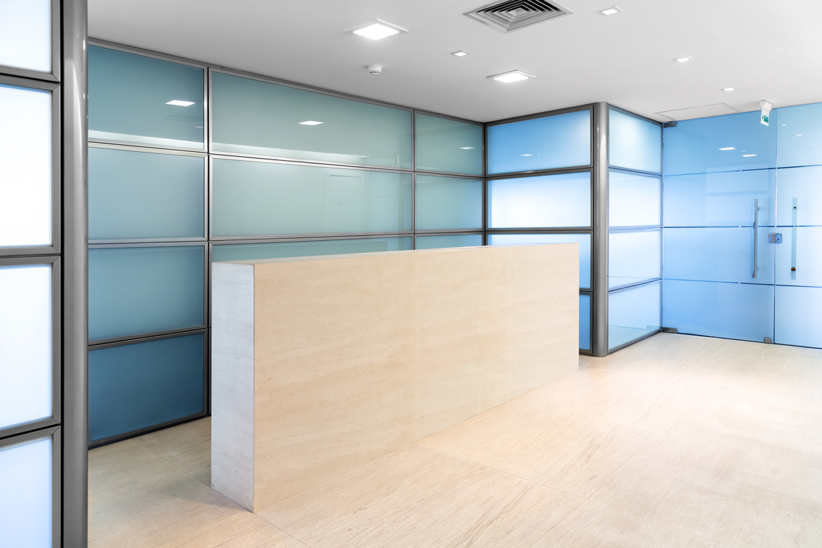 Sala de reunião corporativa com mesa central, divisórias de vidro e iluminação embutida.
