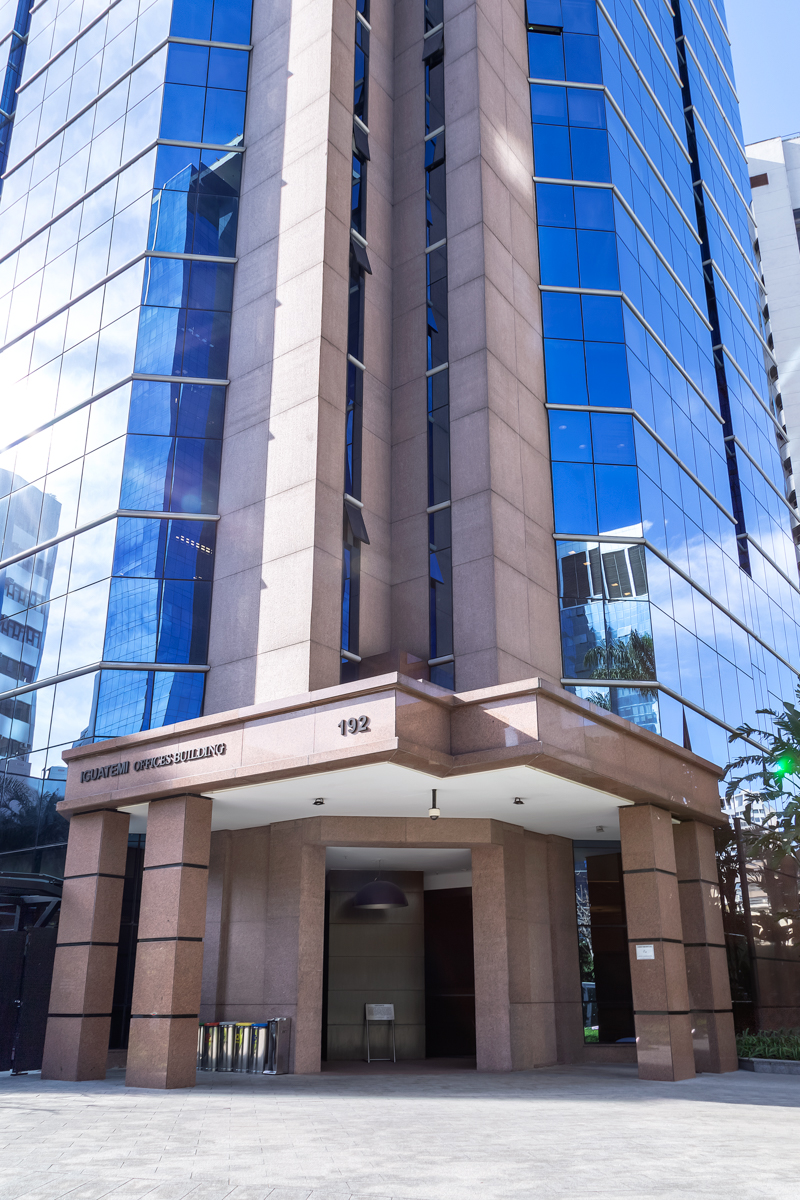 Fachada vertical de edifício corporativo com vidro azul e revestimento em pedra.