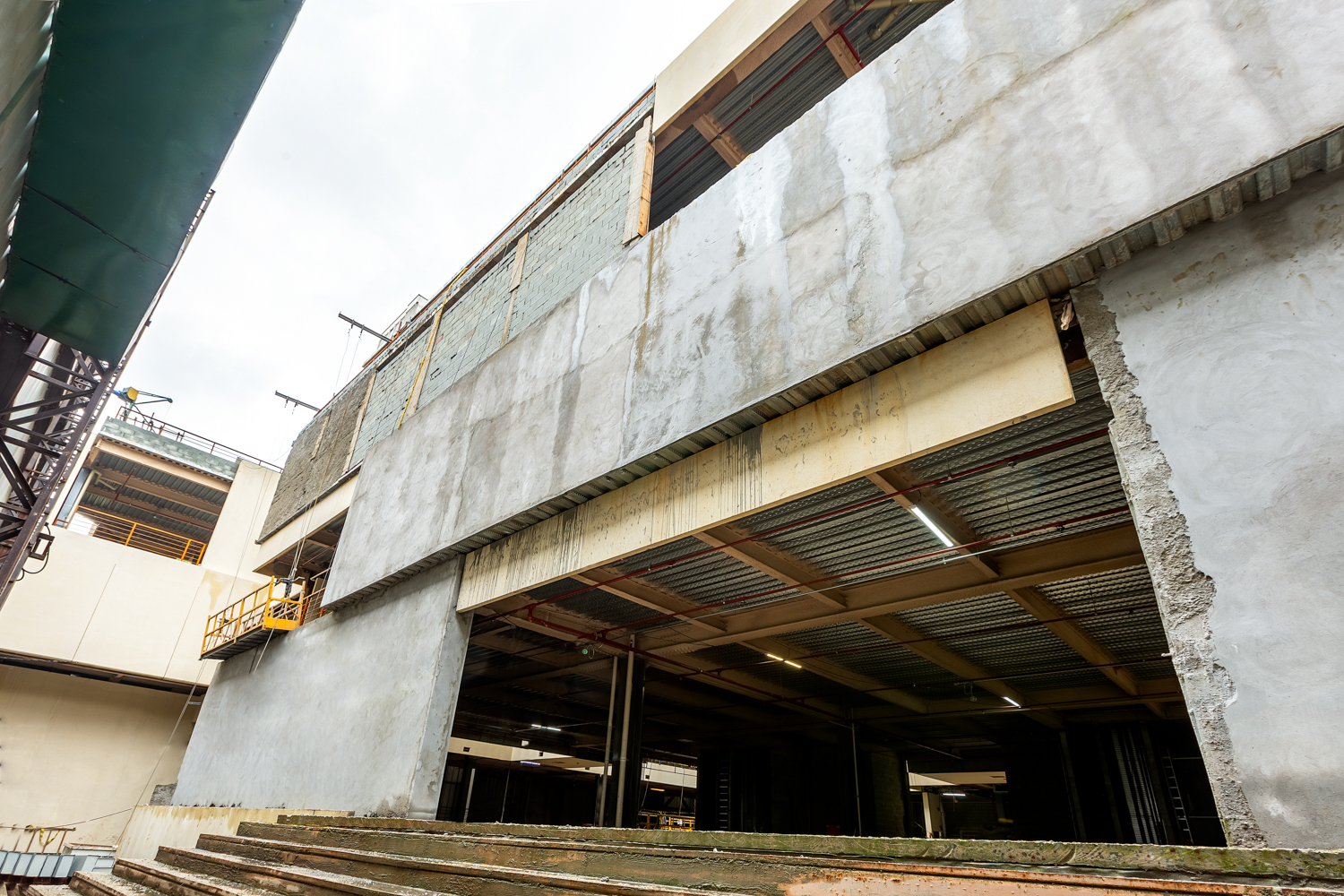Vista externa de edifício em construção com estrutura de concreto e elementos metálicos.