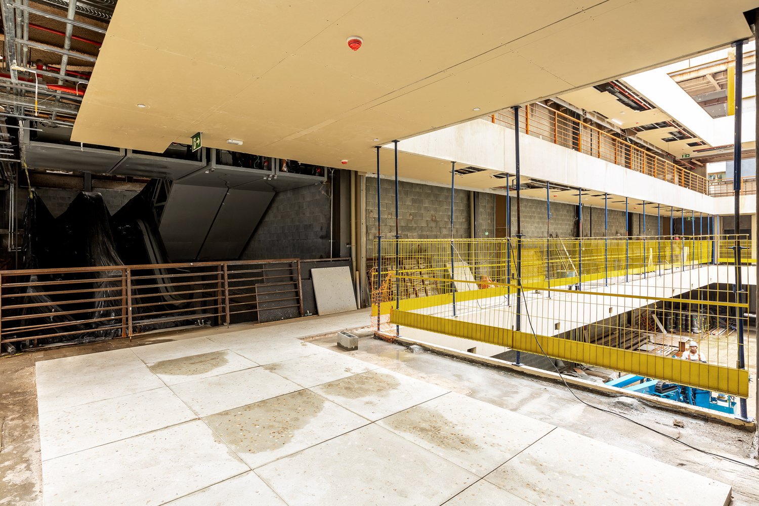 Área de circulação coberta de edifício comercial com pilares e guarda-corpo amarelo.