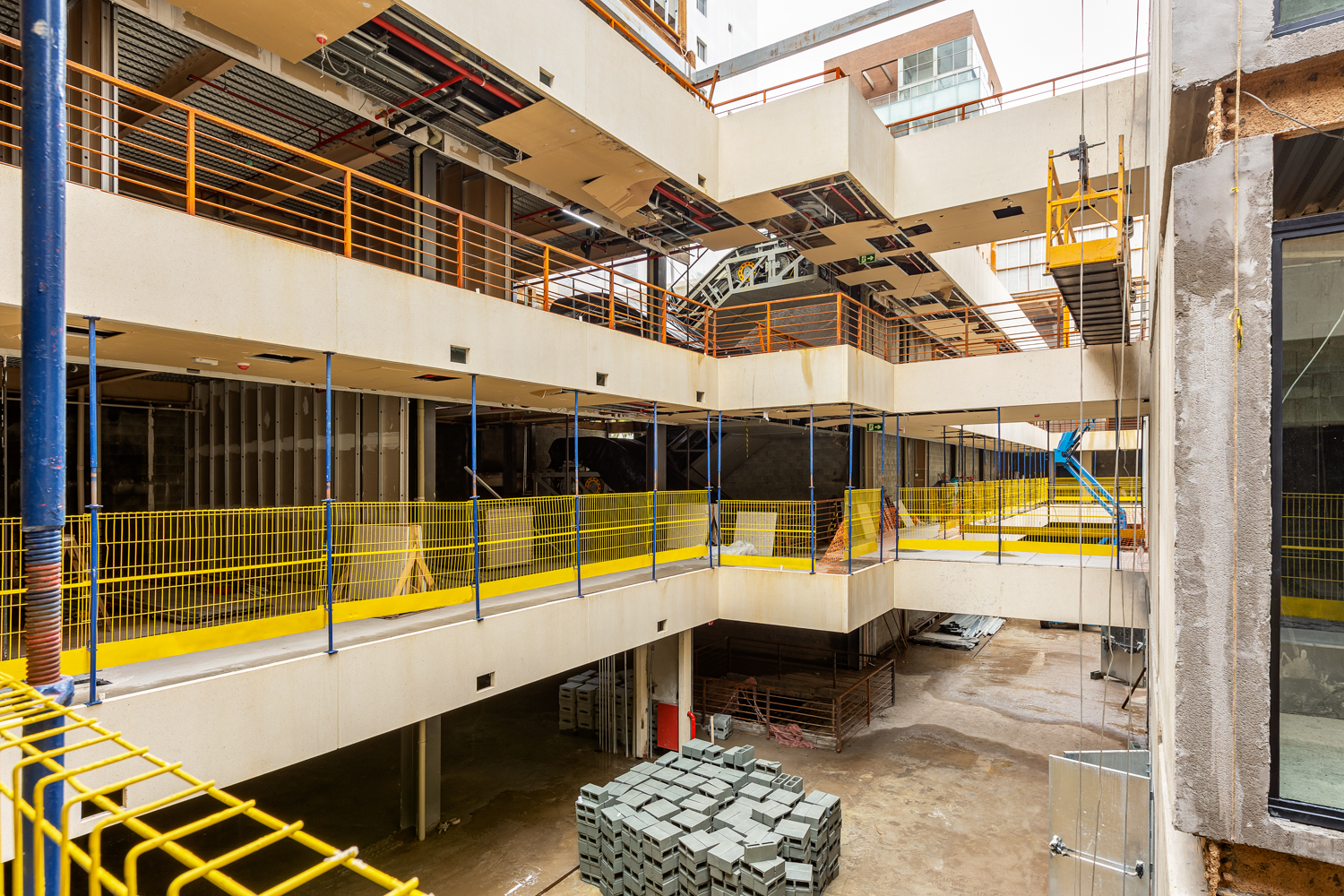 Pátio interno de complexo comercial com passarelas, estrutura aparente e iluminação natural.