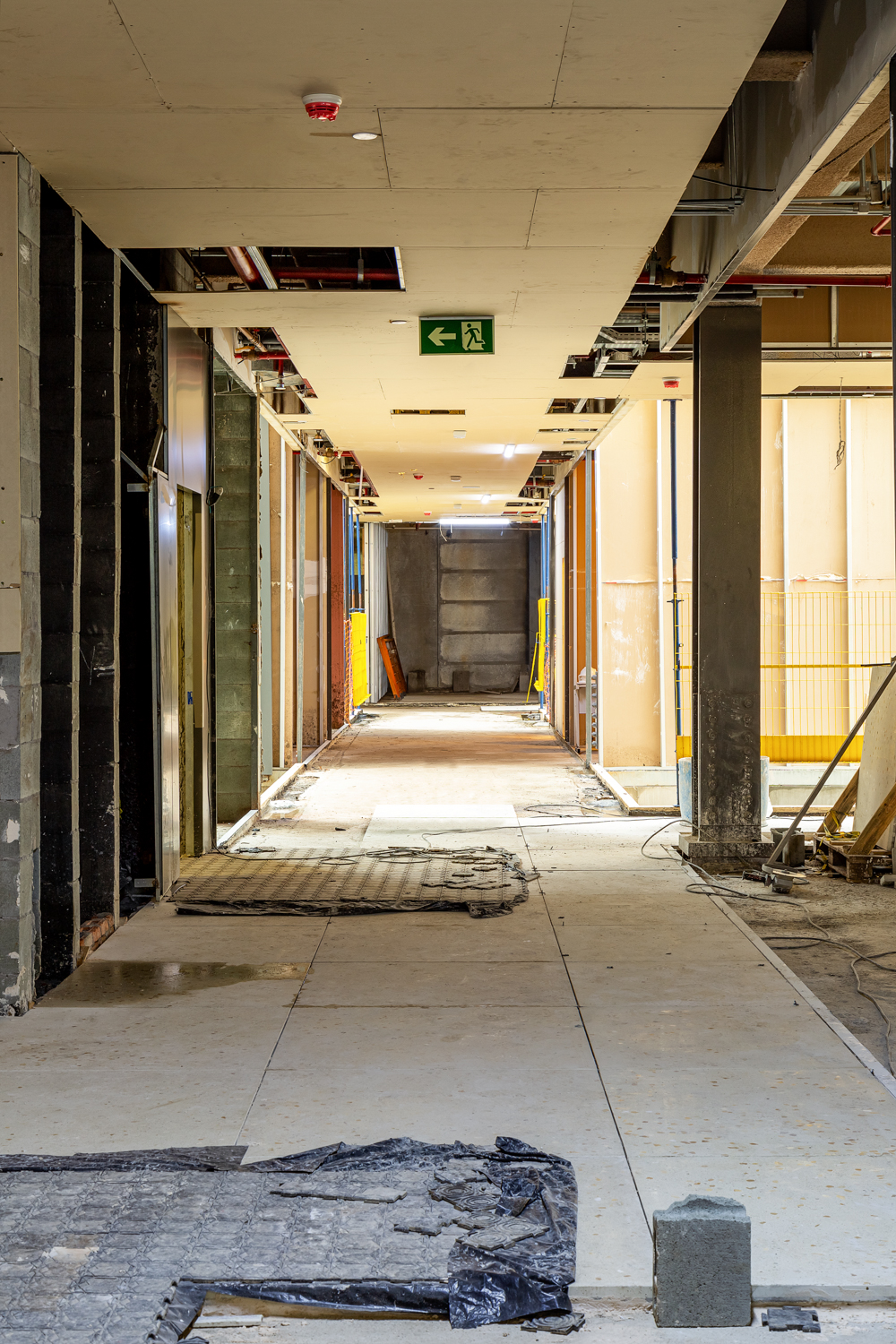 Corredor interno de edifício em fase de acabamento com portas e instalações aparentes.