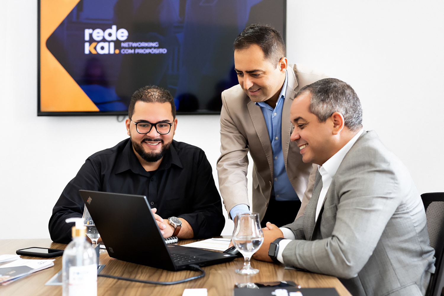 Três profissionais reunidos à mesa durante uma reunião em ambiente corporativo